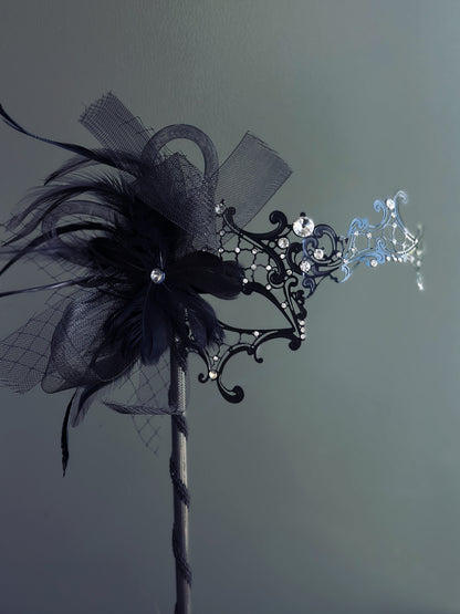 Handheld black masquerade mask with black feathers and rhinestone accents

