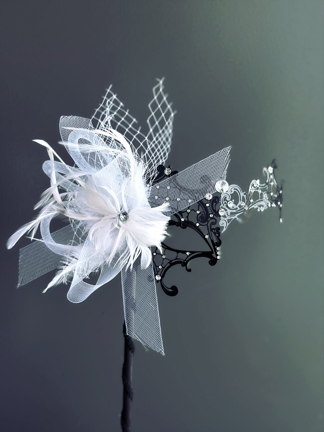 Handheld black metal masquerade mask with white feathers and rhinestone detailing