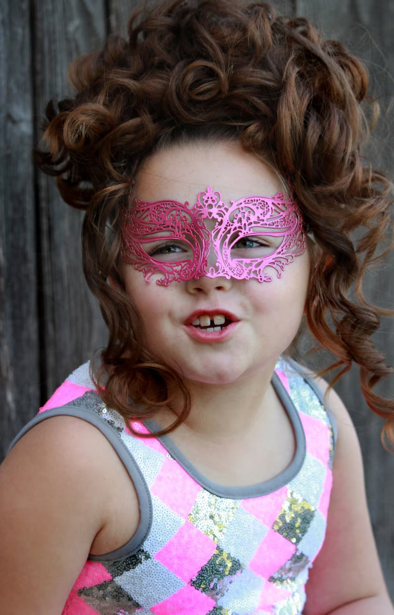 Child wearing metallic pink masquerade mask with ornate filigree design.