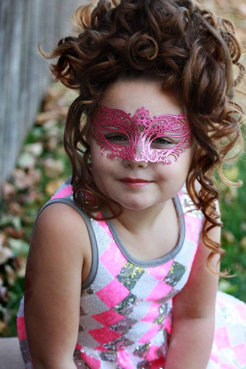 Child wearing metallic pink masquerade mask with ornate filigree design.