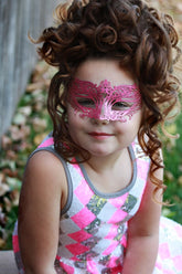 Child wearing metallic pink masquerade mask with ornate filigree design.