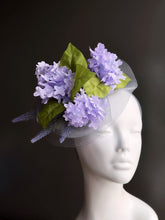 Fascinator hat with lavender flowers, green leaves, and tulle base on mannequin