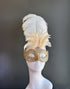 Gold masquerade mask with crystal embellishments and ivory feathers for Venetian ball and gala occasions.