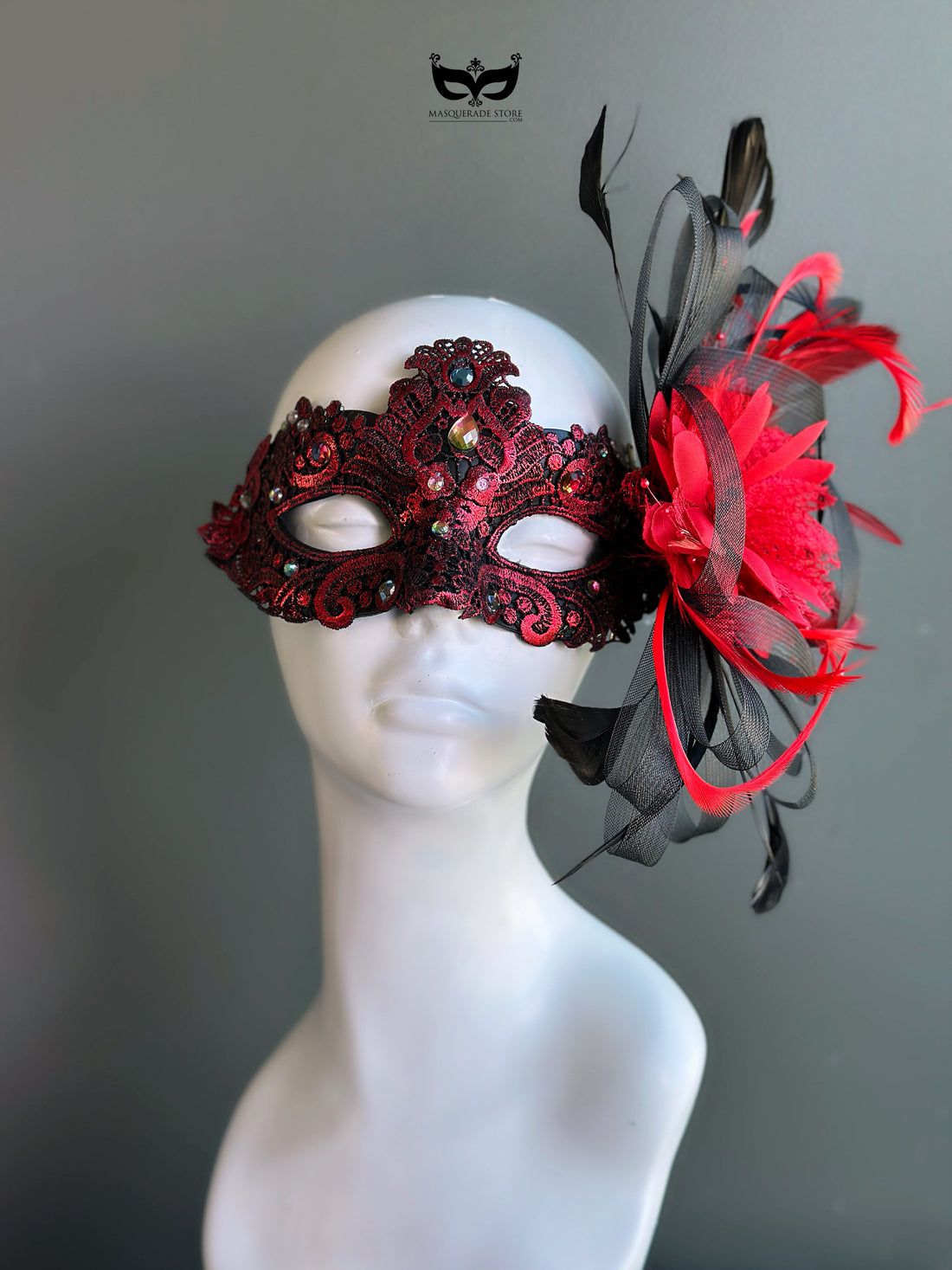 Red lace masquerade mask with crystal details and black feather accent styled for masquerade balls and evening galas.