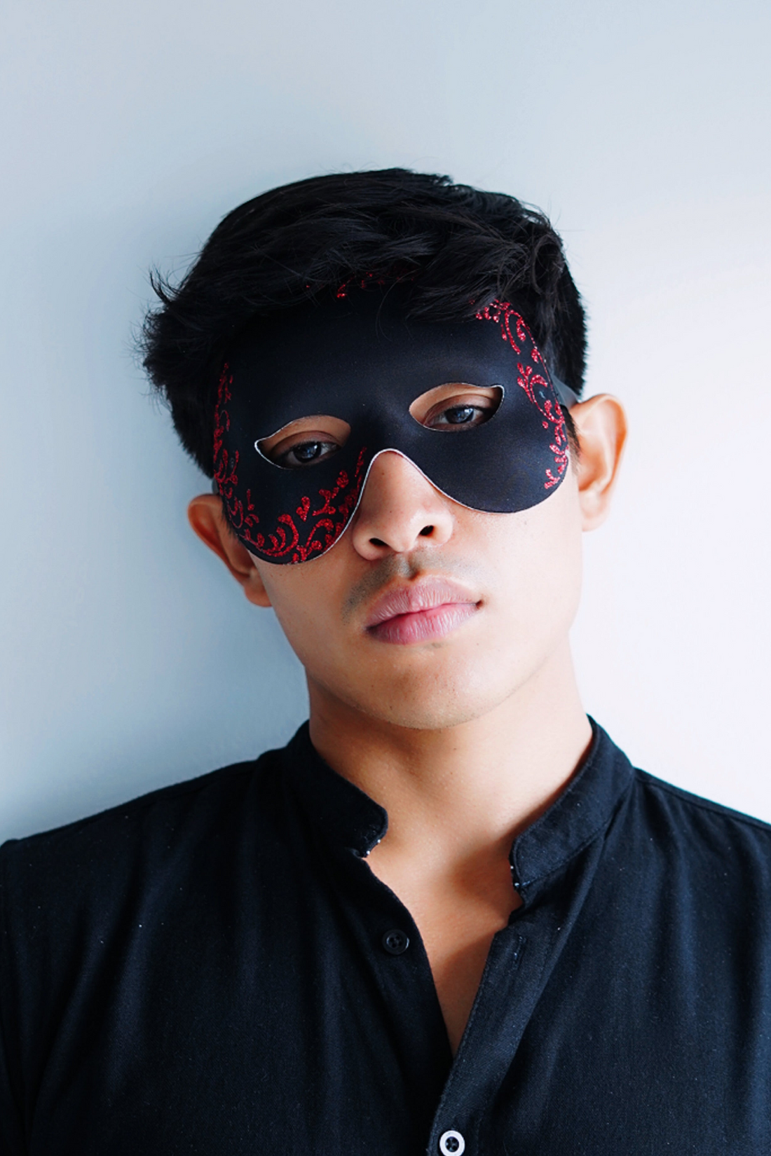 Black base masquerade mask with red filigree glitter details.