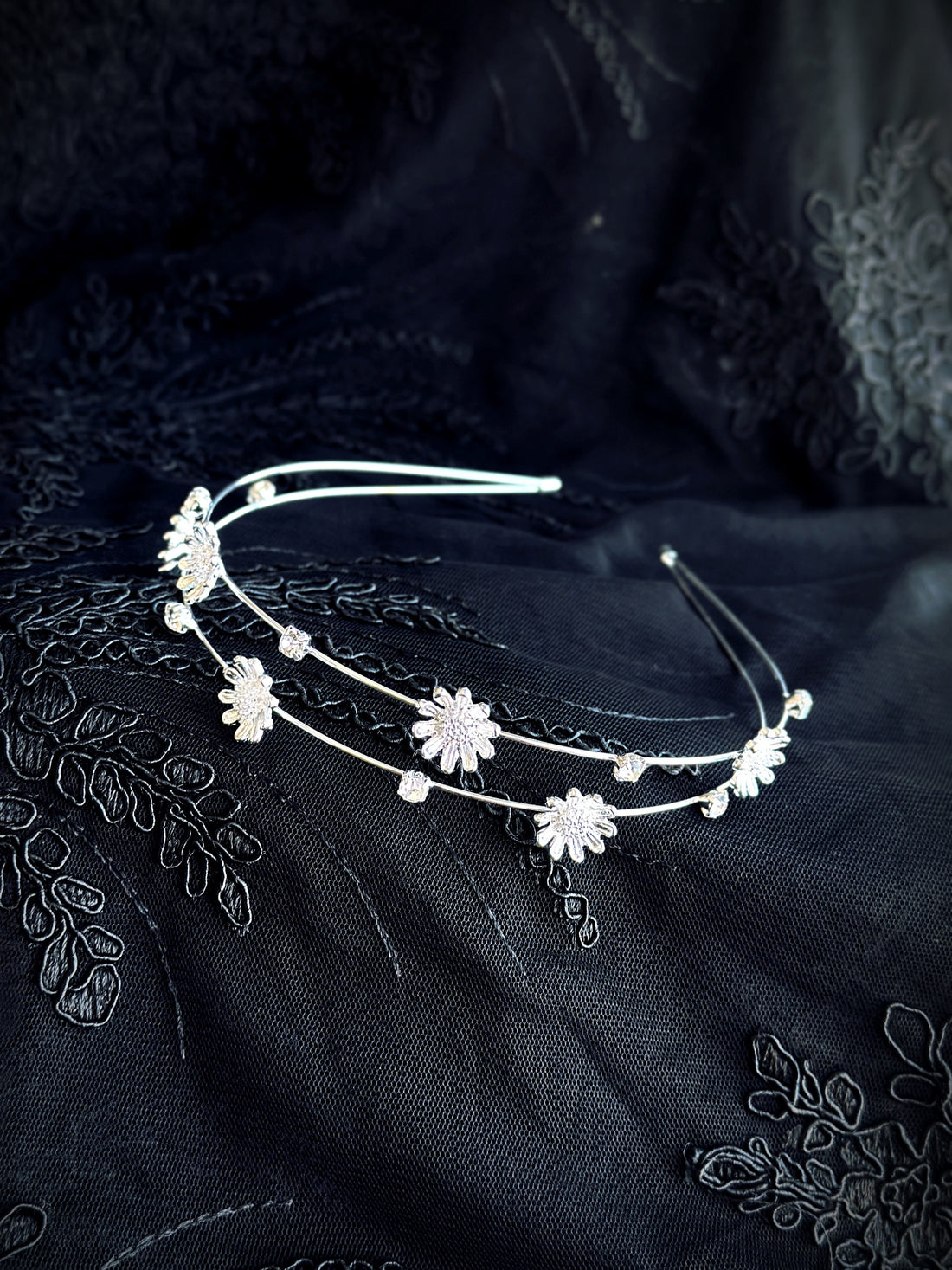 Silver floral headband with daisy-shaped charms and crystals on black embroidered fabric