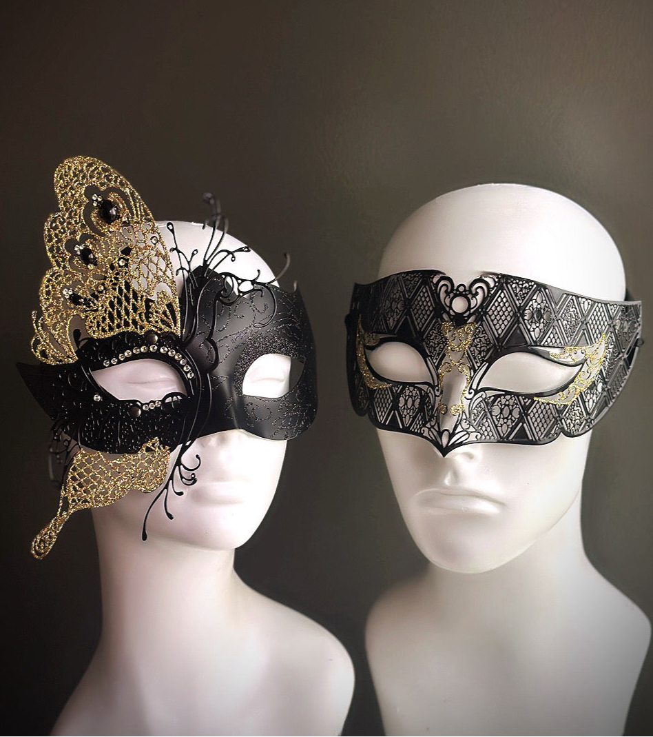 Black and gold couples masquerade masks, one with butterfly lace and gems, the other with filigree lattice and gold accents

