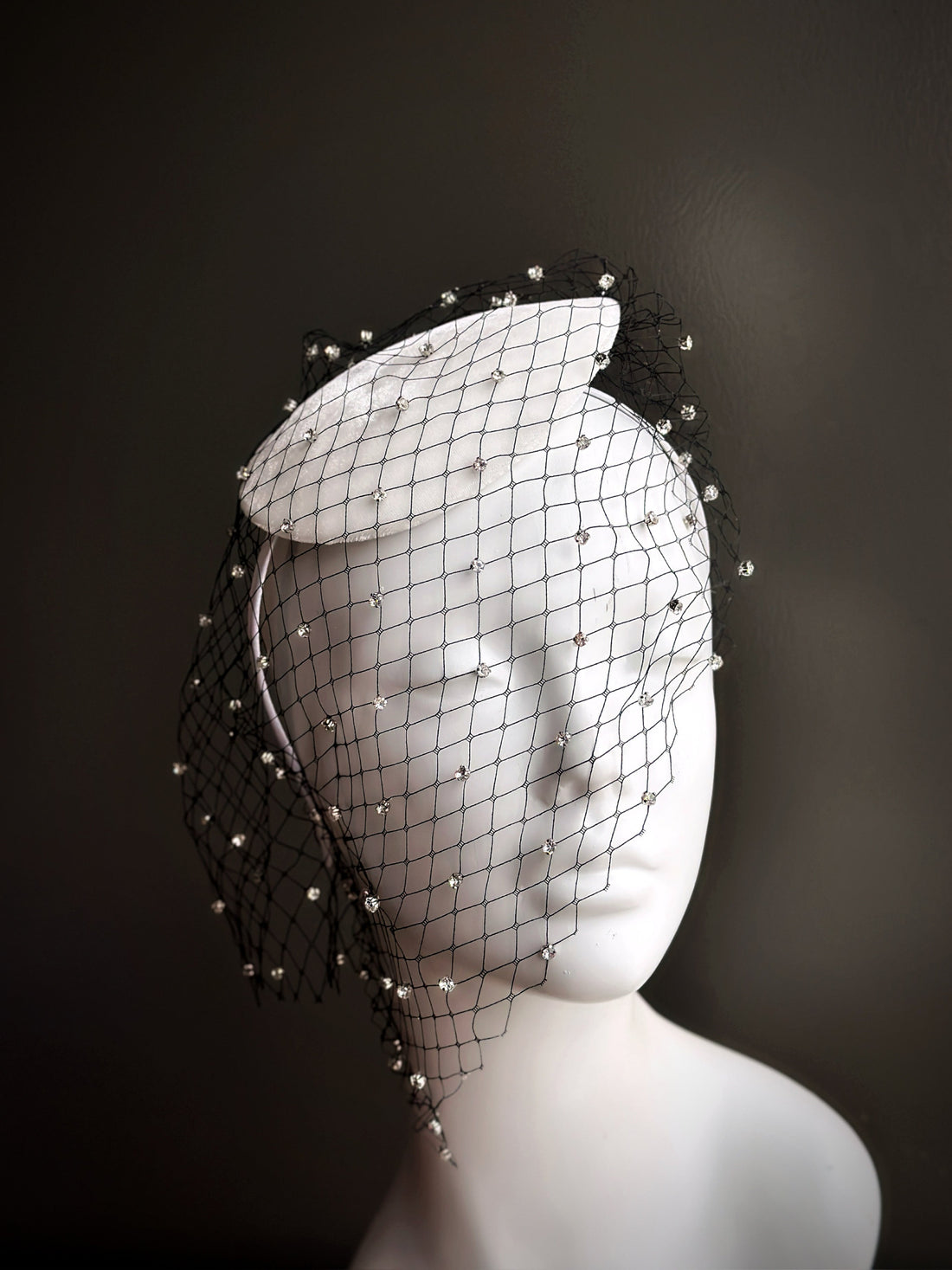 White fascinator hat with black rhinestone veil.