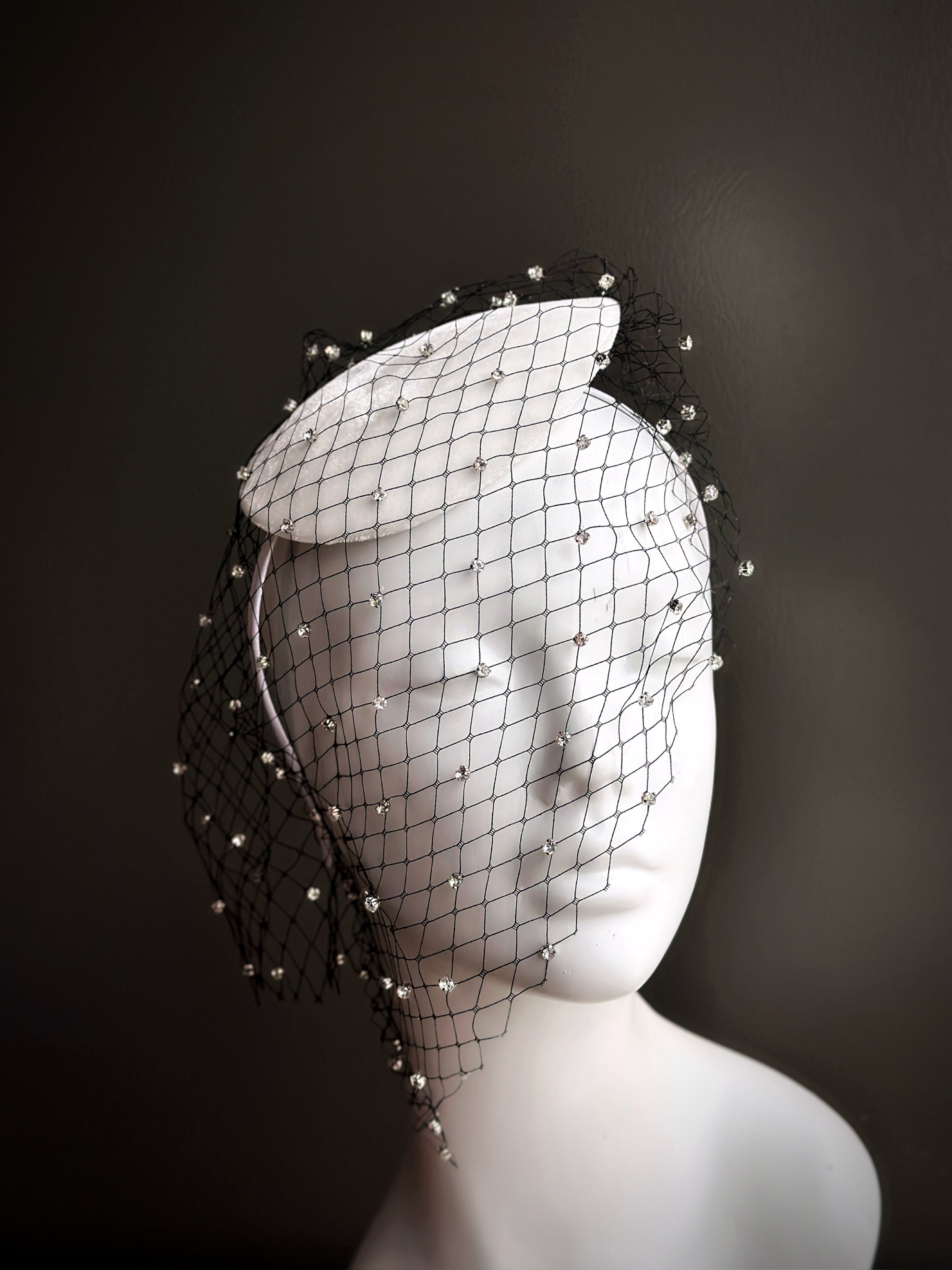 White fascinator hat with black rhinestone veil.

