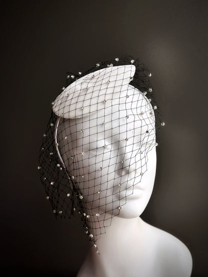 White fascinator hat with black rhinestone veil.


