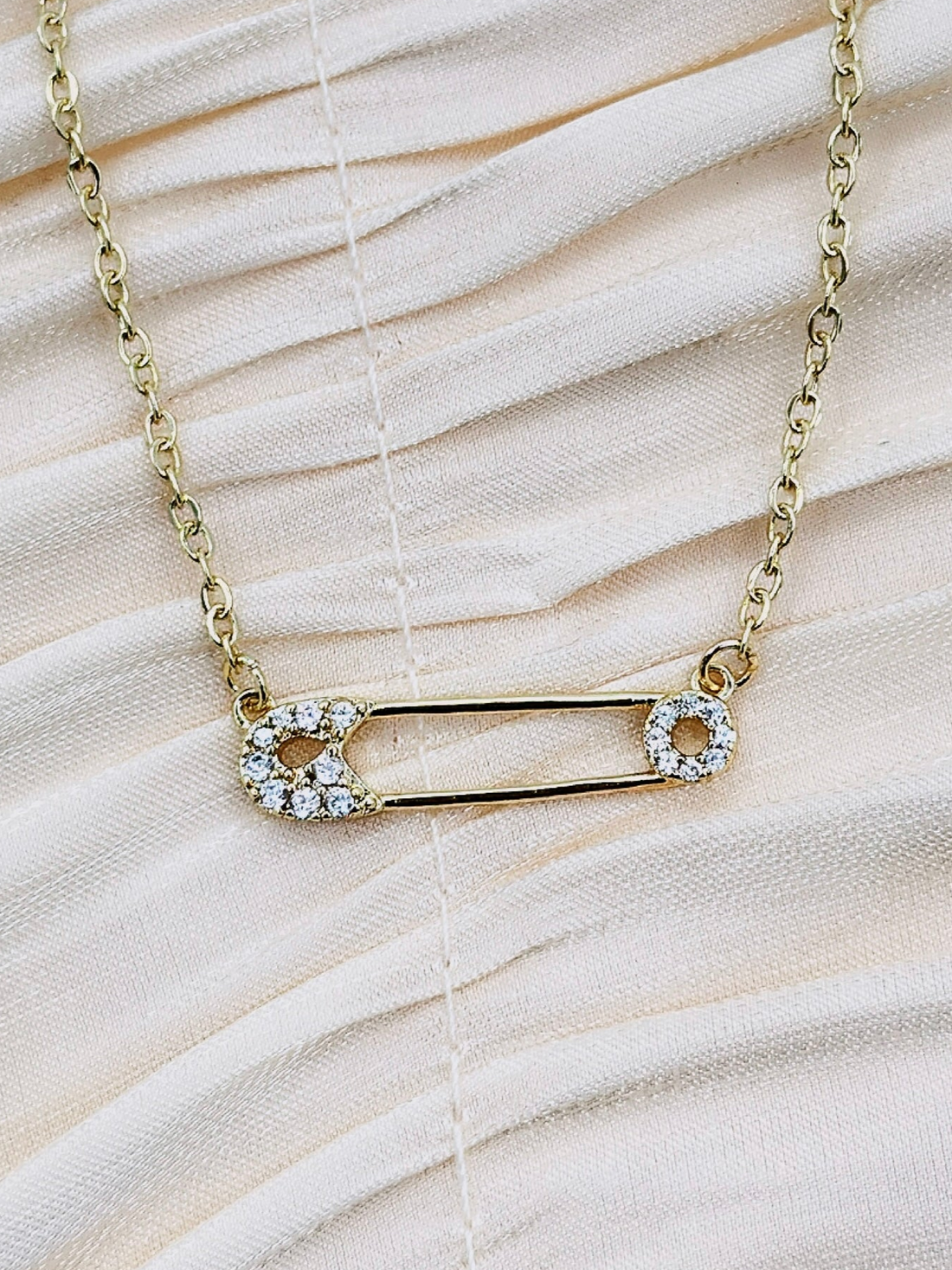 Gold safety pin pendant adorned with sparkling stones on a gold-plated chain.
