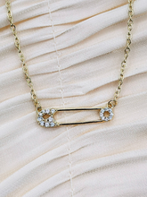 Gold safety pin pendant adorned with sparkling stones on a gold-plated chain.
