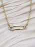 Gold safety pin pendant adorned with sparkling stones on a gold-plated chain.
