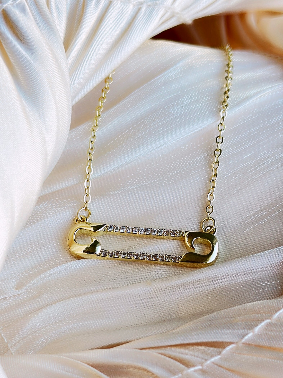 Gold plated necklace with a gold safety pin pendant adorned with clear crystals.
