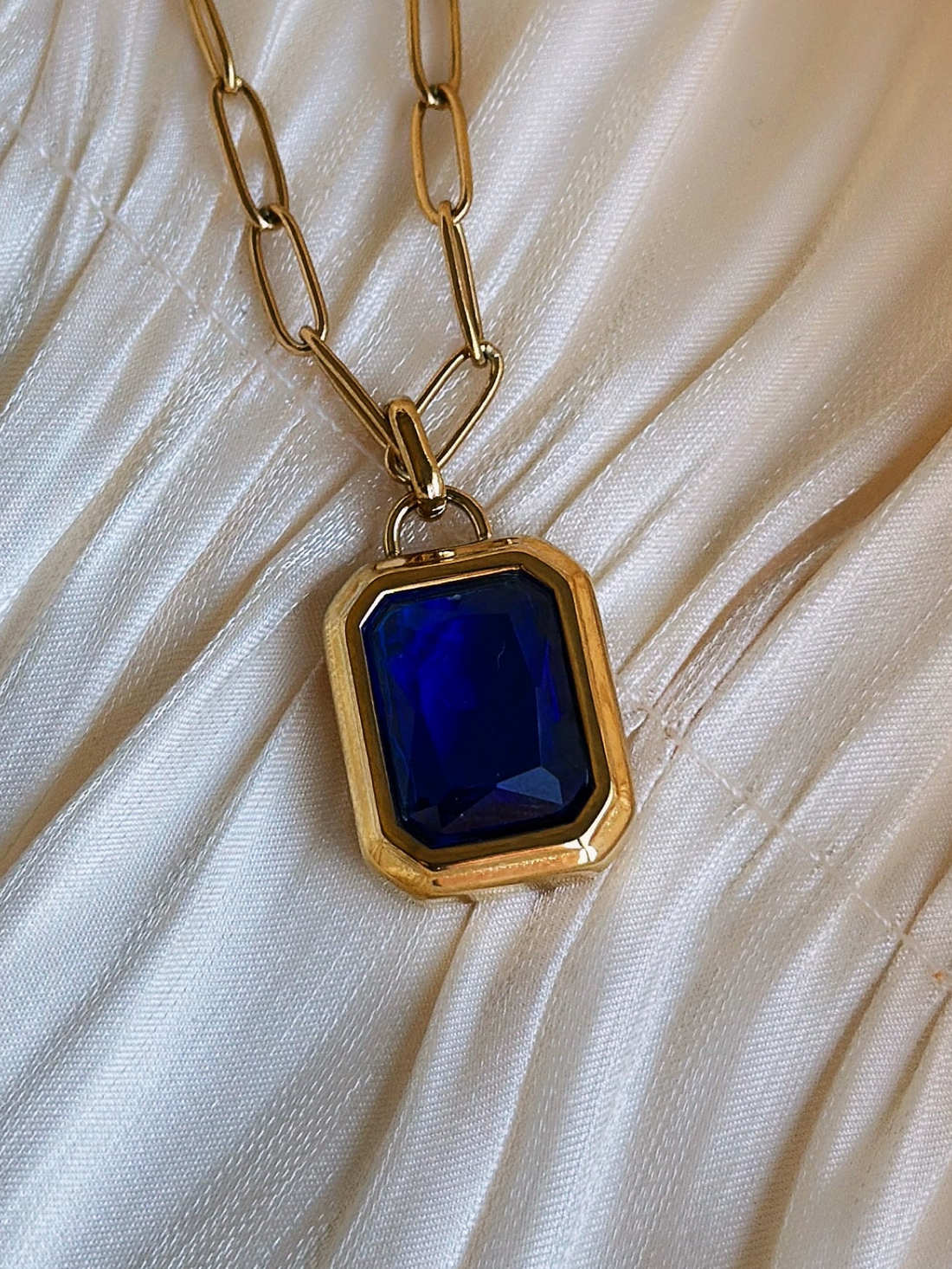 Gold necklace with a blue gemstone pendant.