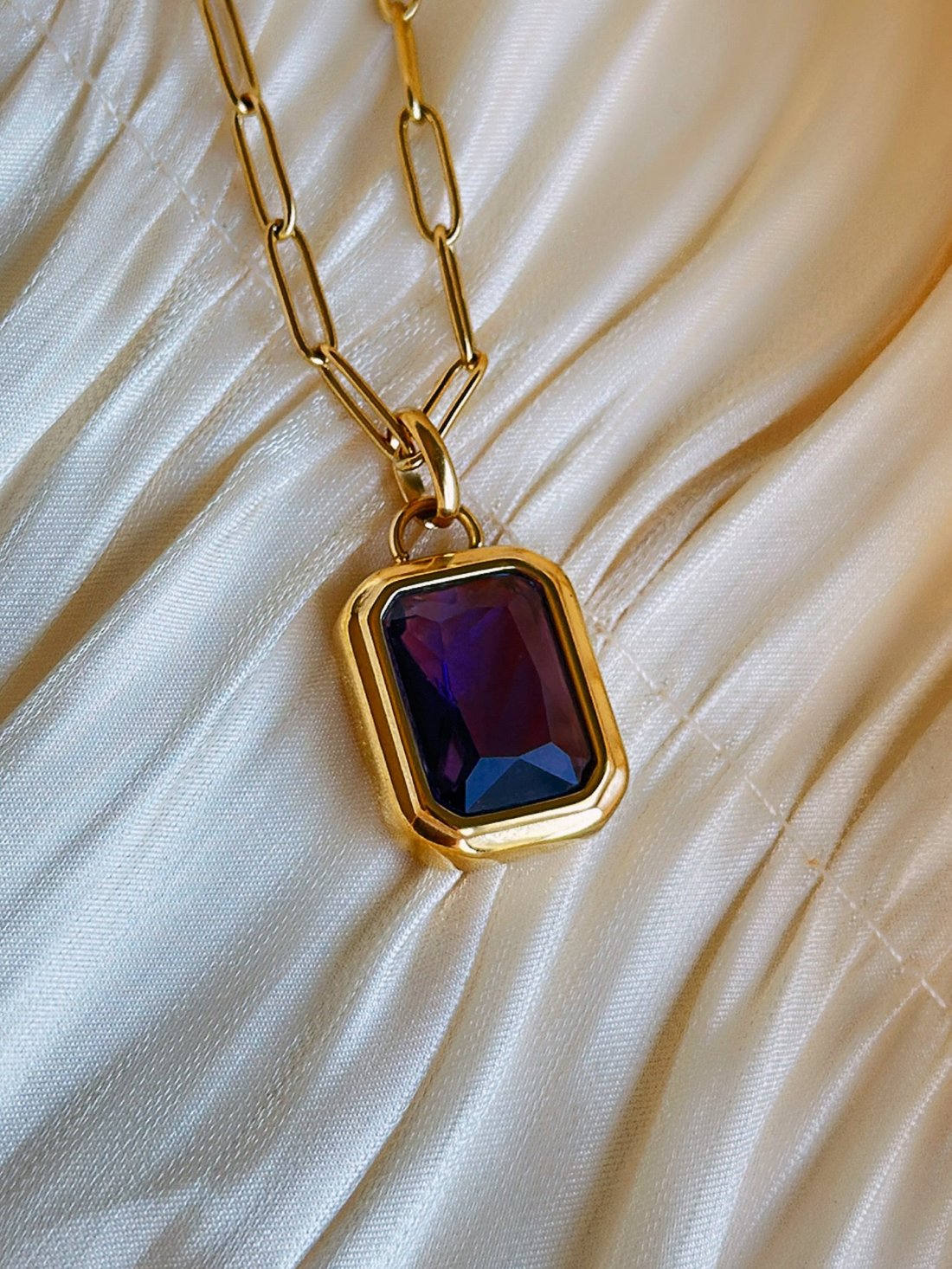 Gold necklace with a purple pendant .