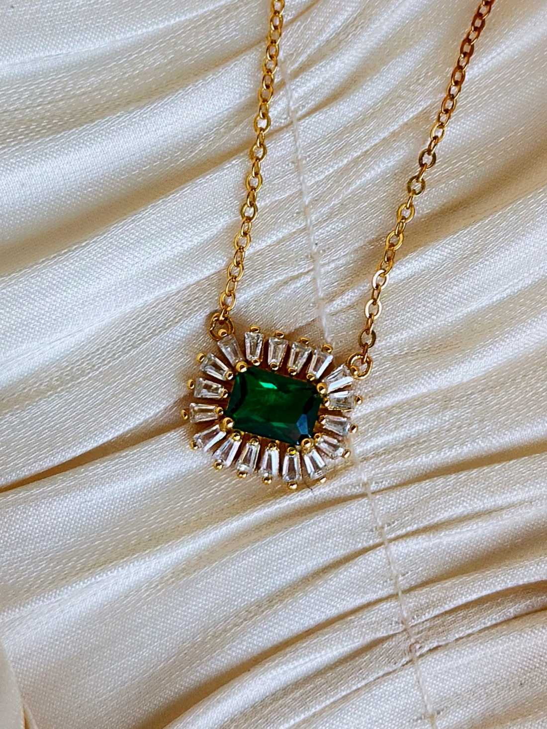 Gold necklace with a green gemstone surrounded by small clear crystals.