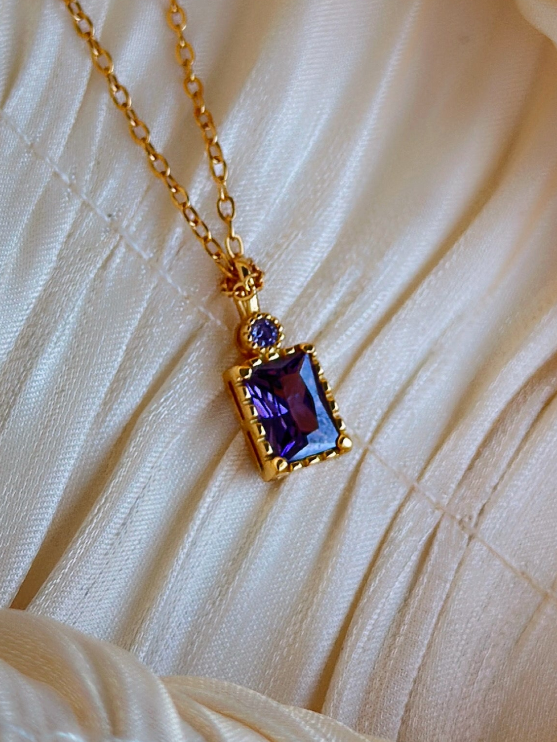 Gold necklace with a purple gemstone pendant.