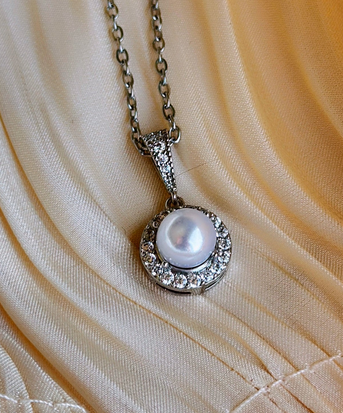 Silver necklace with clear crystals and a pearl in the center.