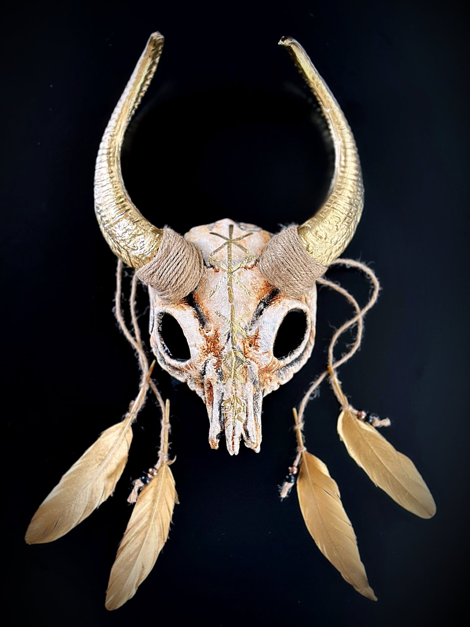 Ram horn skull headdress with gold horns, feathers, and runes