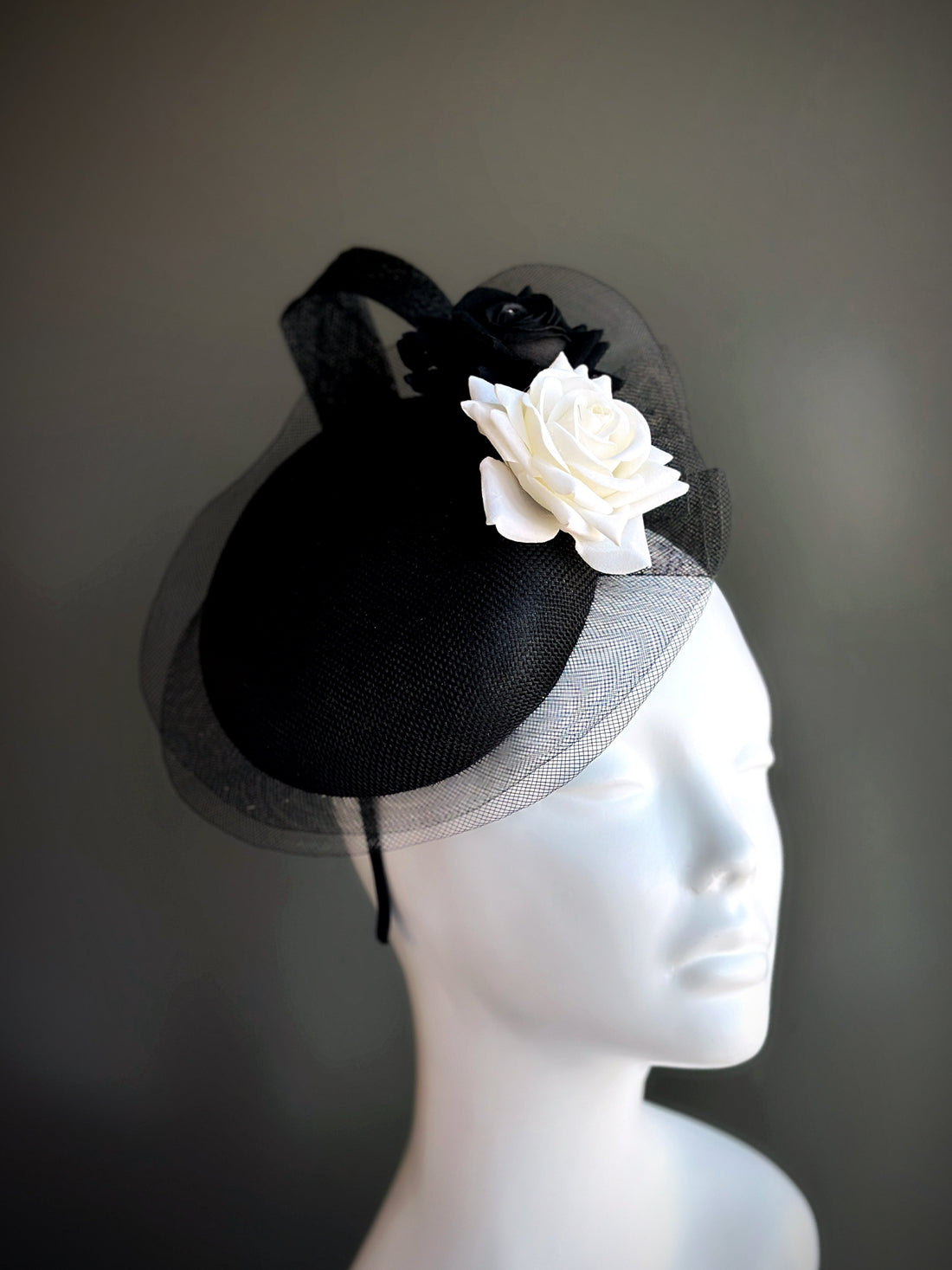 Black fascinator hat with black and white rose, tulle veil, and curved brim.
