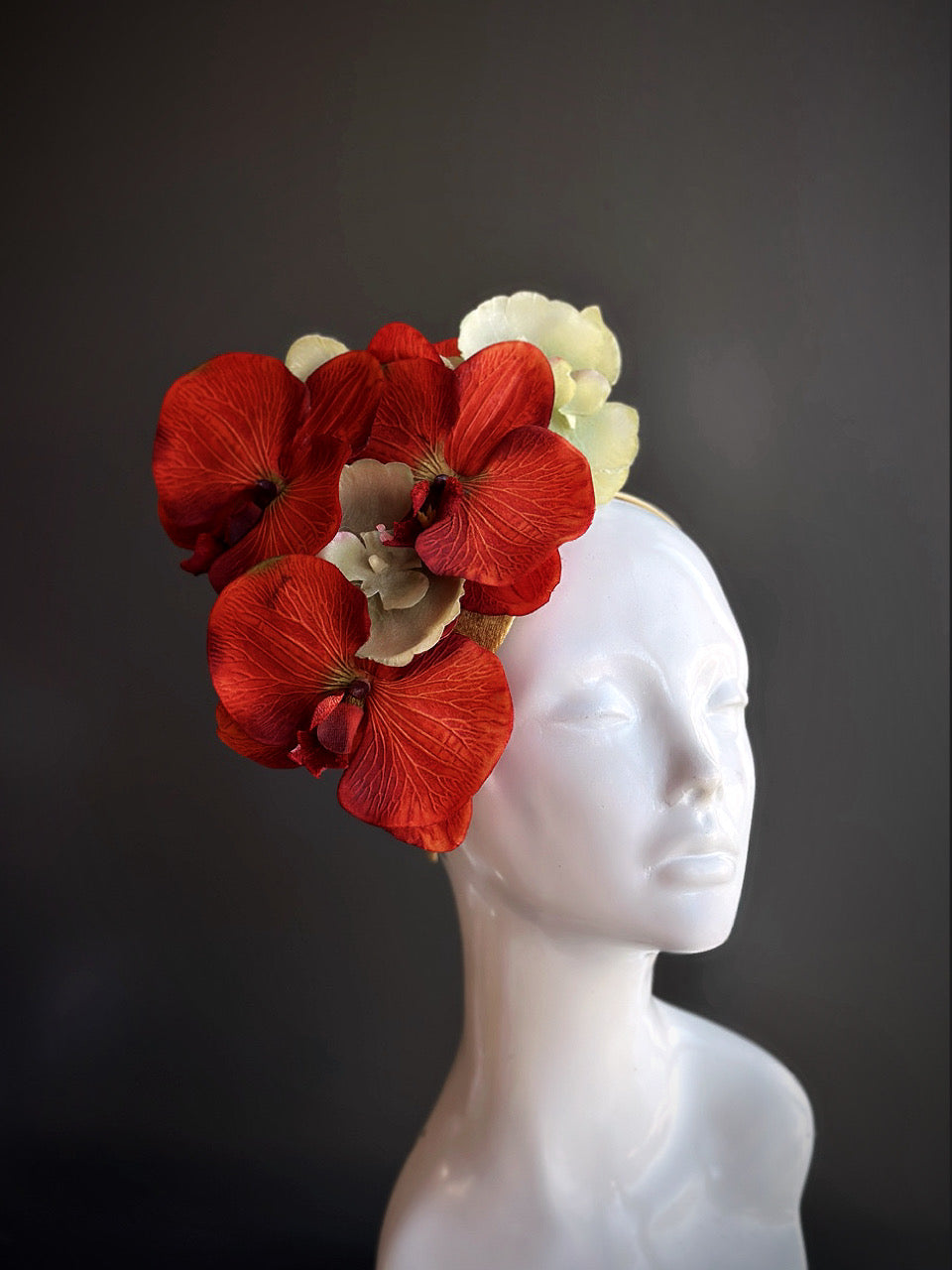 Orange and green orchid fascinator displayed on a mannequin head with a gold headband.