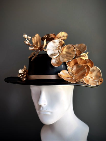 Black statement hat decorated with metallic gold orchid flowers and sculpted floral accents