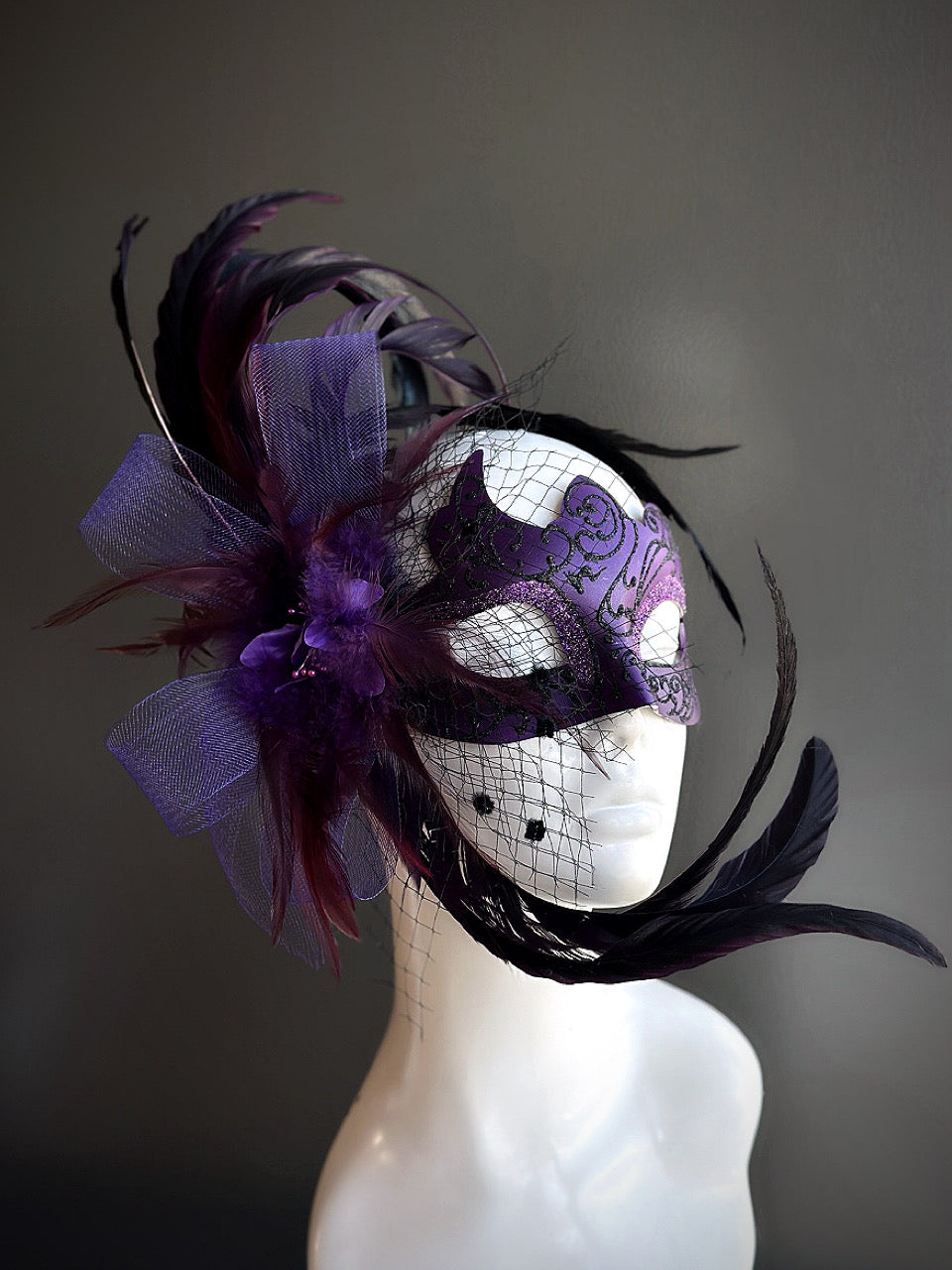 Purple and black feather masquerade mask with a net veil .
