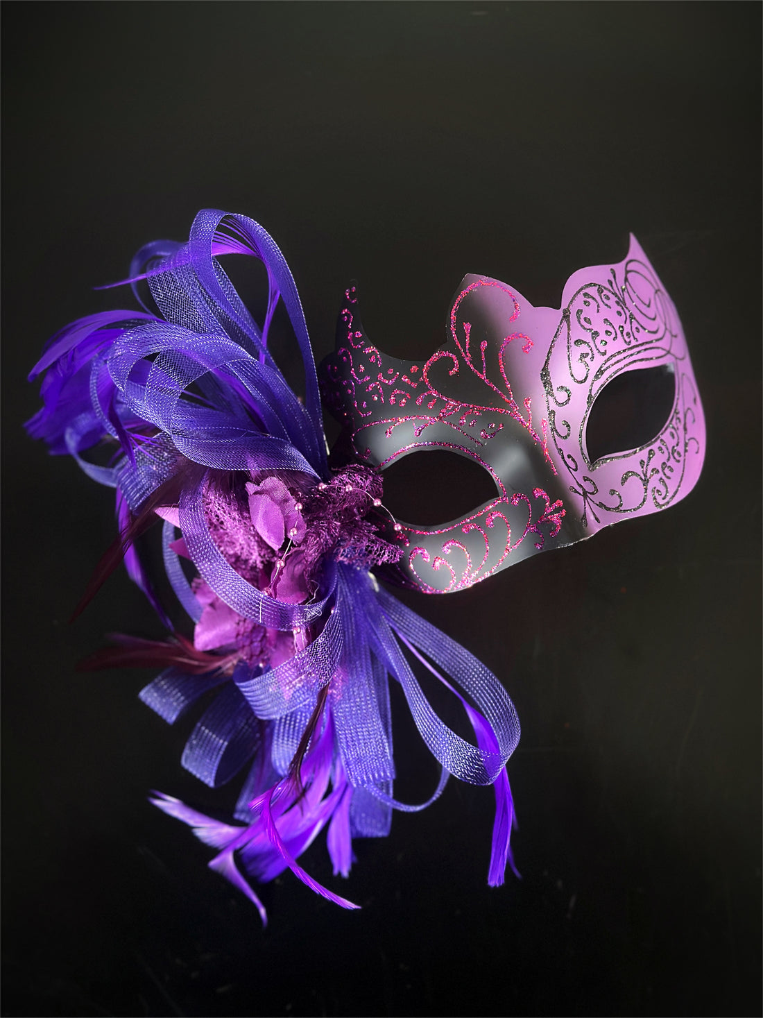 Purple and black masquerade mask with purple feathers, glitter scrolls, and flower accents for women.