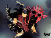 A set of two masks: a devilish red demon mask with horns and a rustic ram mask decorated with feathers and twine, ideal for Halloween or cosplay.