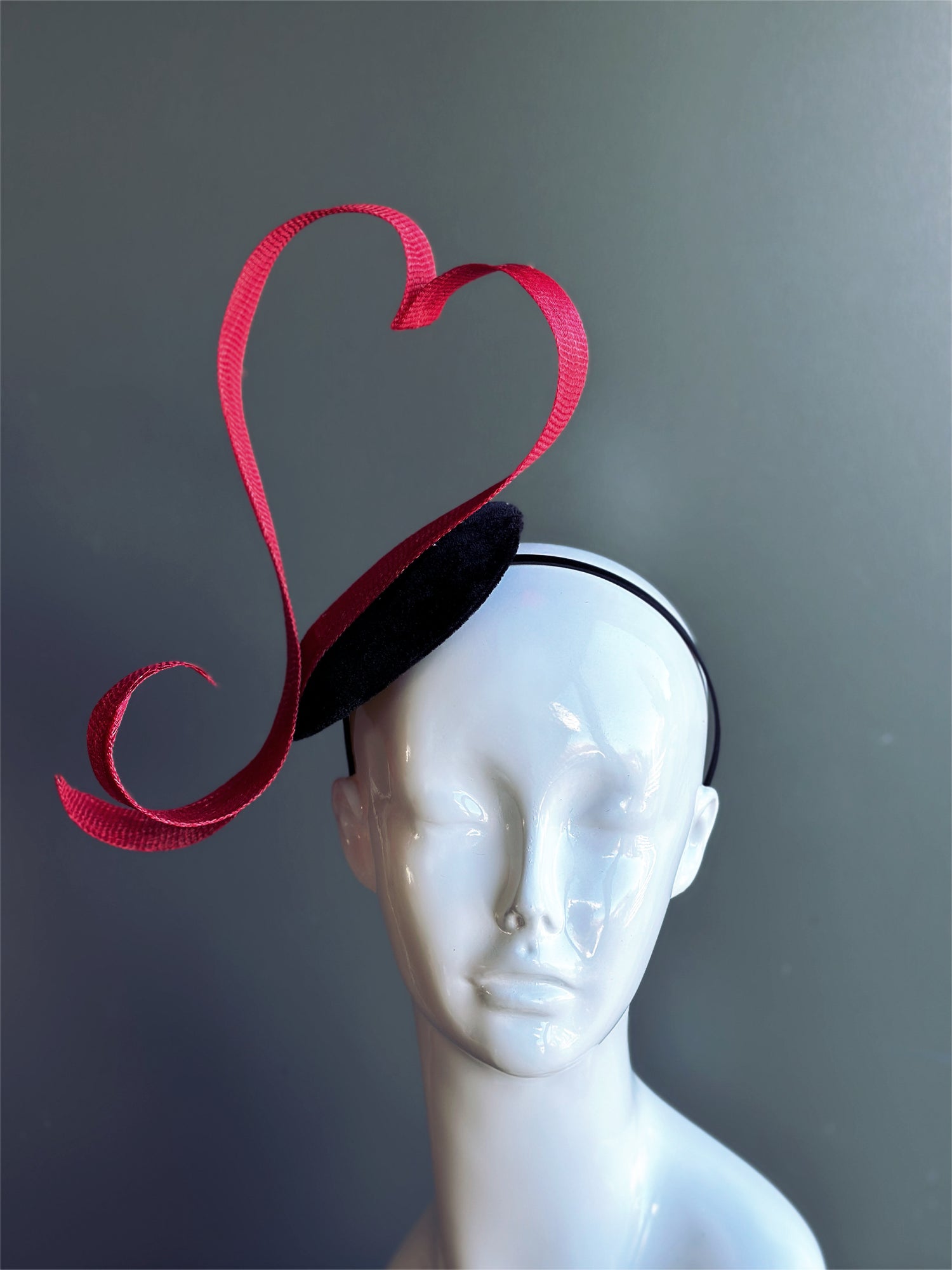 Red heart fascinator hat with sculpted ribbon design.
