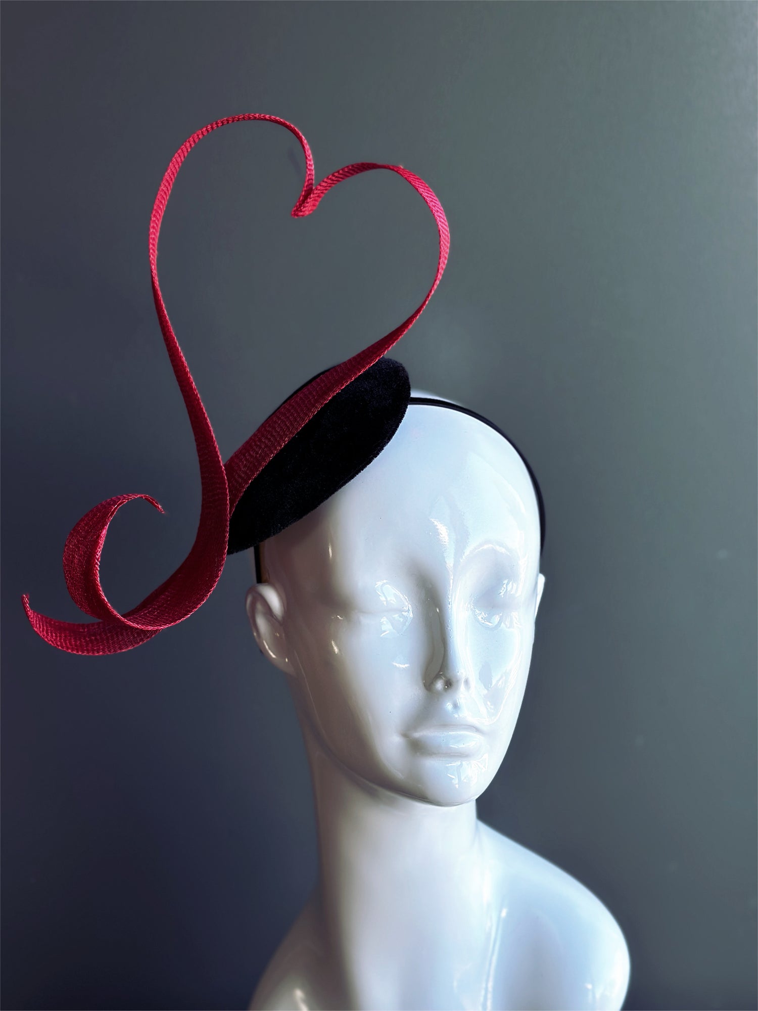 Red heart fascinator hat with sculpted ribbon design.