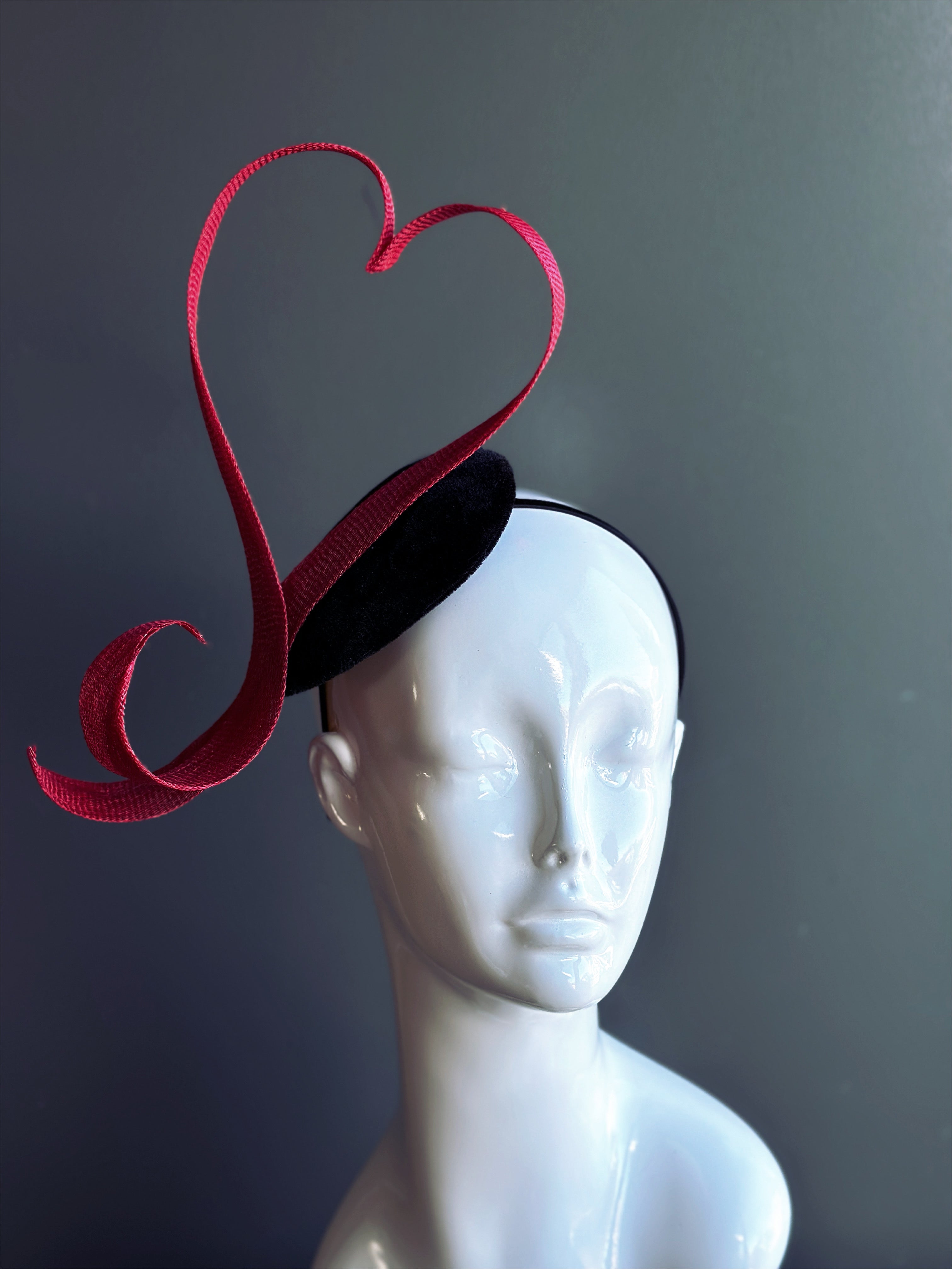 Red heart fascinator hat with sculpted ribbon design.