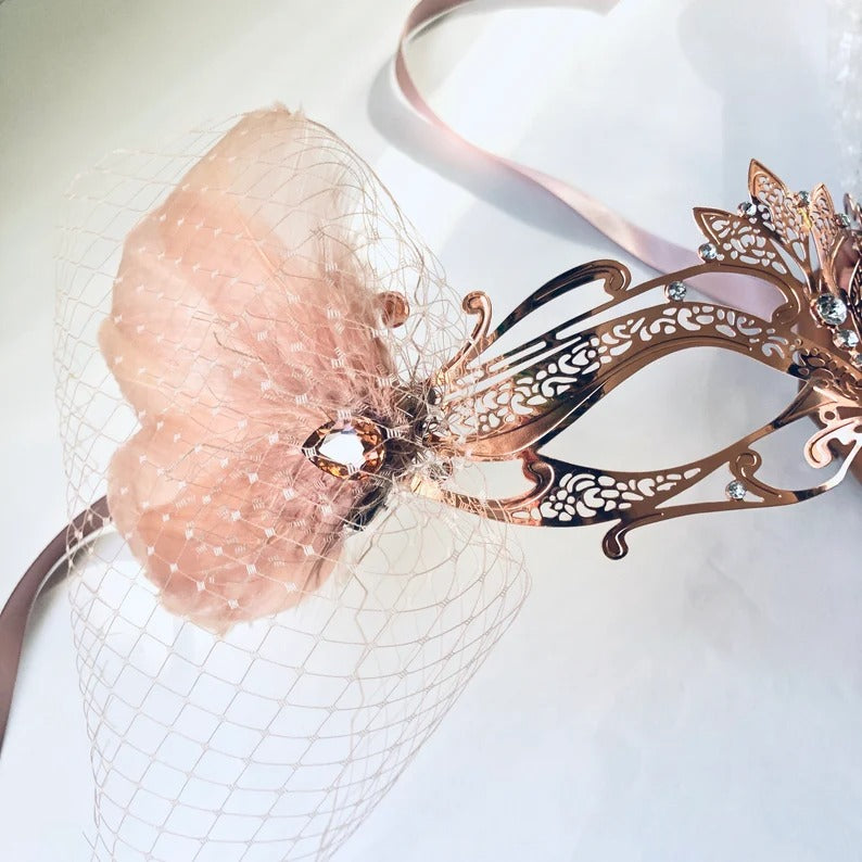 Elegant rose gold masquerade mask with filigree design, flower, netting, and rhinestones for weddings, Venetian balls, and prom parties.