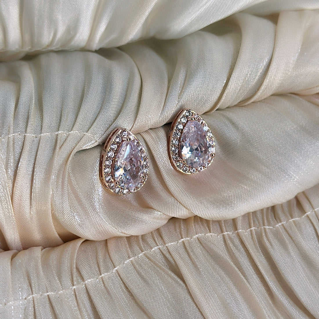 Rose gold pear-shaped cubic zirconia stud earrings with a halo setting, designed for a sophisticated and radiant look.