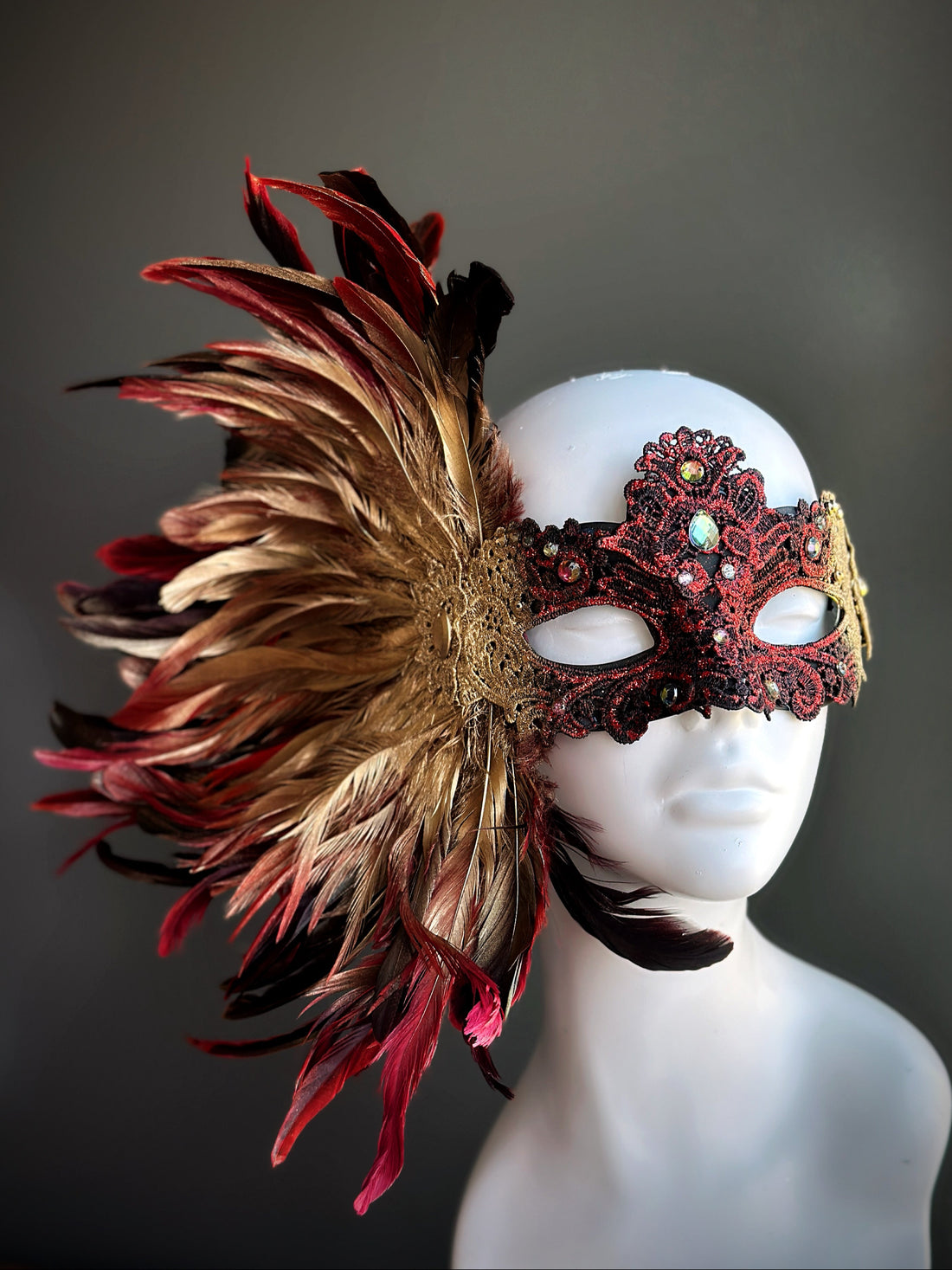 Red and gold feather masquerade mask with opulent plume design and ornate lace accents.