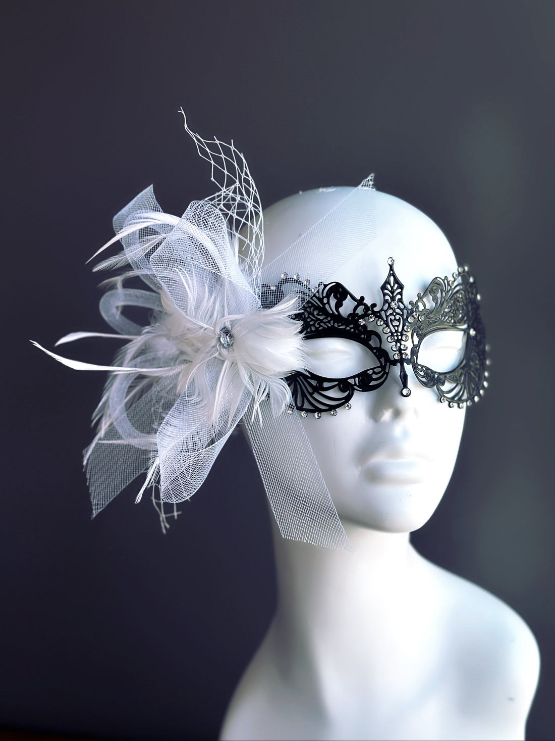 Elegant black filigree masquerade mask with white feathers and mesh ribbon on a mannequin