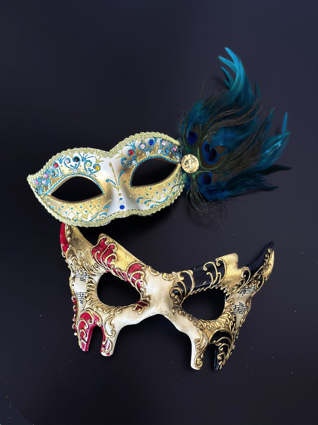 Red and gold baroque music scroll mask paired with a jeweled peacock feather mask in blue and green for a masquerade event or Mardi Gras