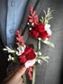 A stunning artificial floral boutonniere and corsage set in shades of red, green, and white.