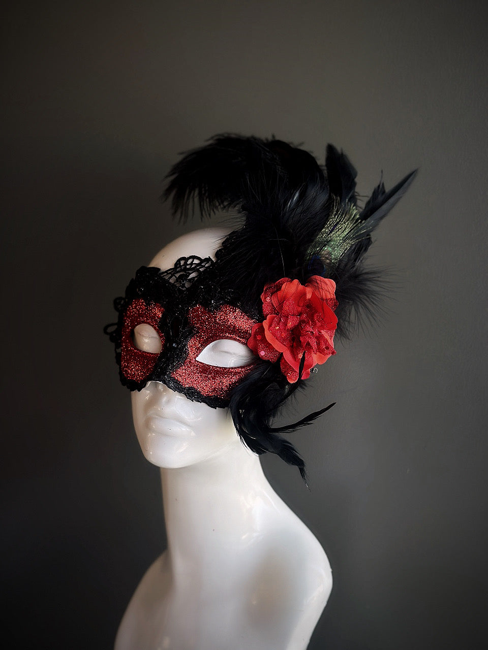 Red and black mask with lace details, bold feathers, and a red rose accent for a dramatic and elegant design.