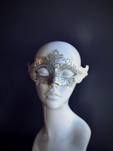 Silver metal masquerade mask with intricate filigree and rhinestone accents displayed on a mannequin head.

