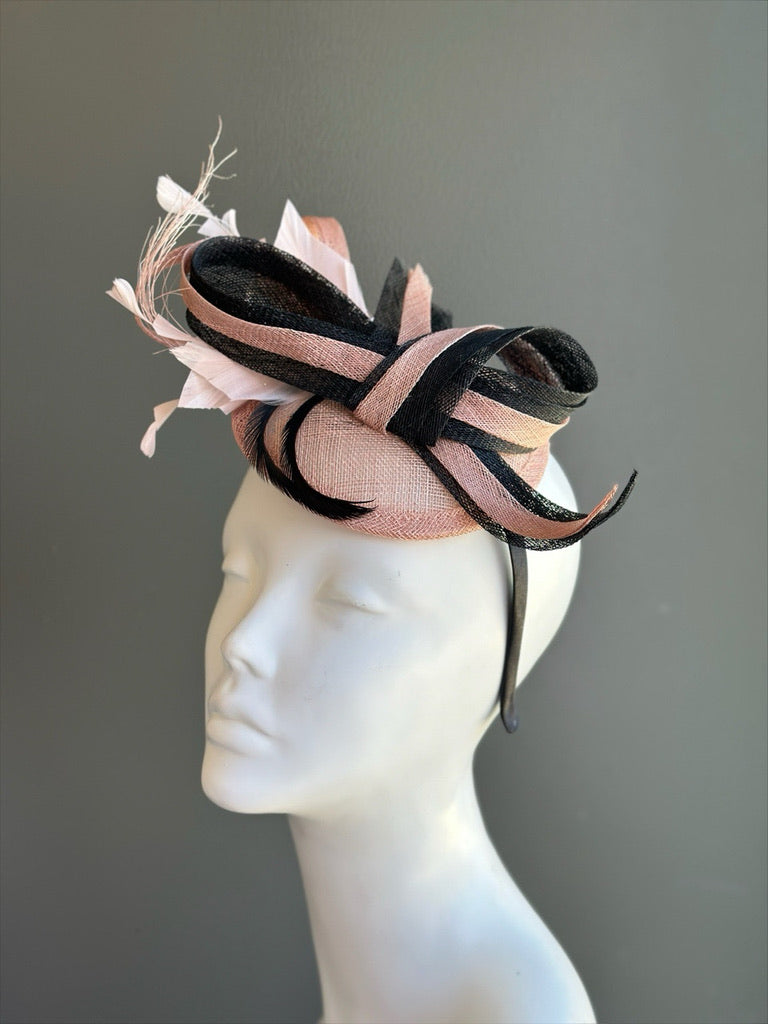 Blush pink sinamay fascinator with black sculpted loops and feather accents for derby and wedding occasions.