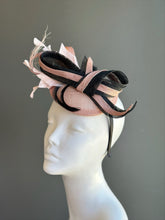 Blush pink sinamay fascinator with black sculpted loops and feather accents for derby and wedding occasions.