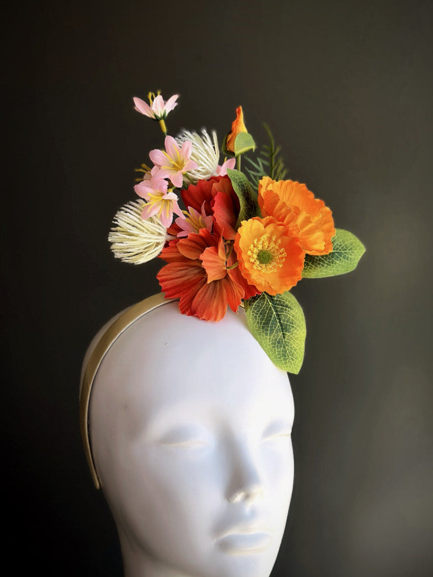 Floral fascinator hat with orange, coral, and pink flowers and green leaves on beige headband

