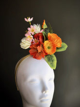 Floral fascinator hat with orange, coral, and pink flowers and green leaves on beige headband

