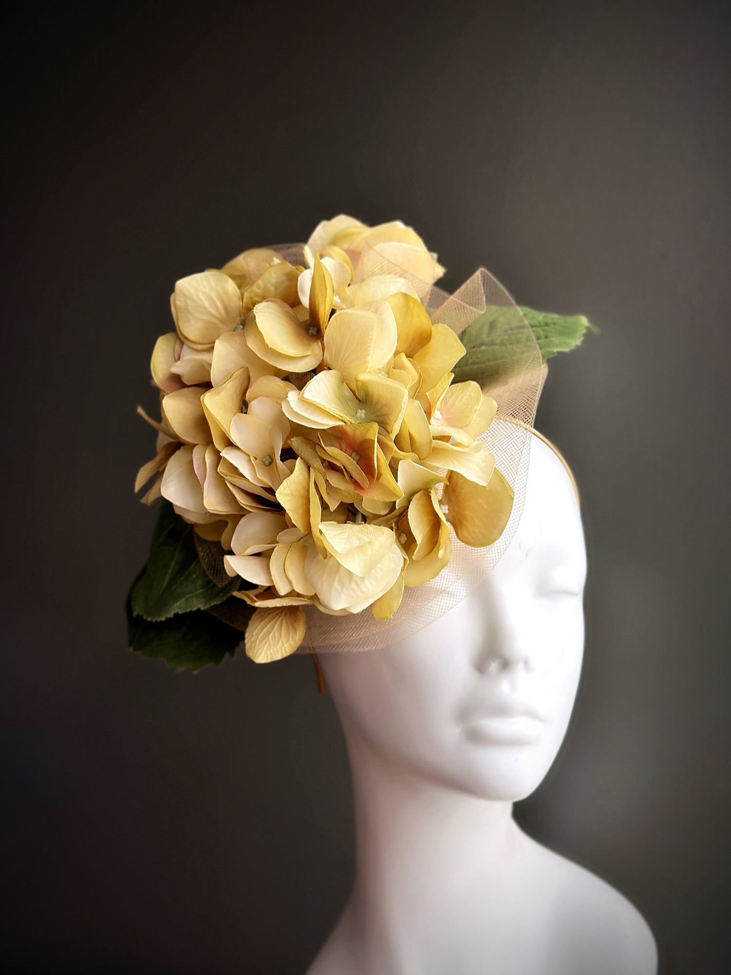 Oversized fascinator hat with yellow hydrangea flowers and green leaves on mannequin

