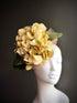 Oversized fascinator hat with yellow hydrangea flowers and green leaves on mannequin


