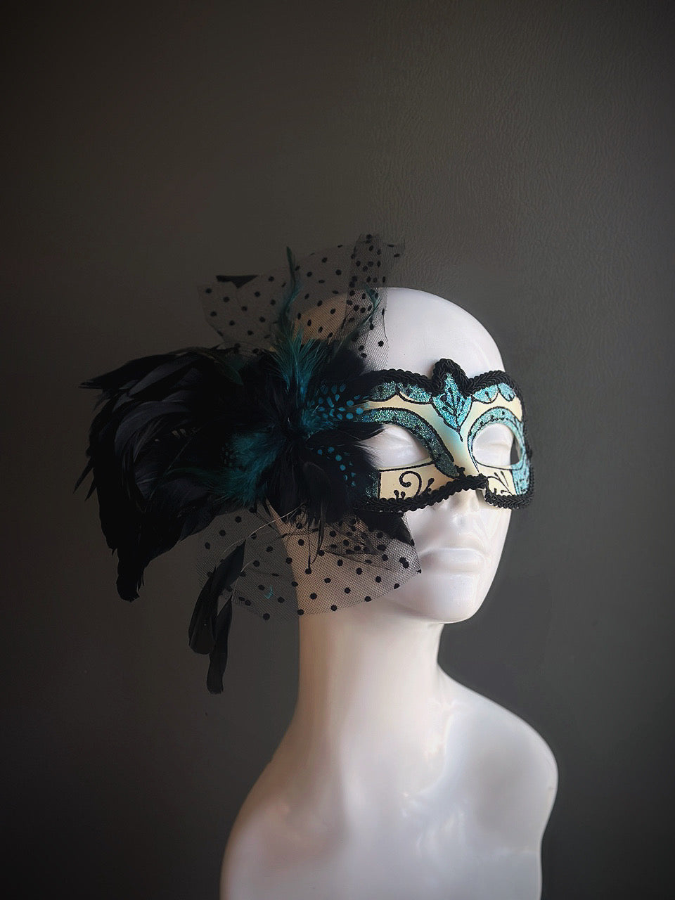 Teal and black mask with lace details, bold feathers, and dotted tulle accents, offering a dramatic and sophisticated design.
