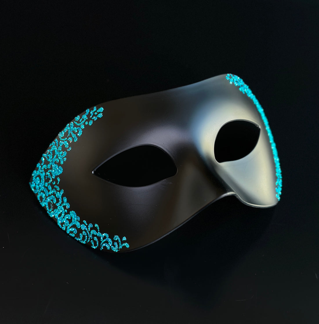 Matte black Venetian Phantom masquerade mask with turquoise glitter filigree trim, lightweight half-face costume mask for masquerade balls, Mardi Gras, Halloween, Venetian carnival, cosplay, weddings, black-tie events, theatrical performances, and formal parties.
