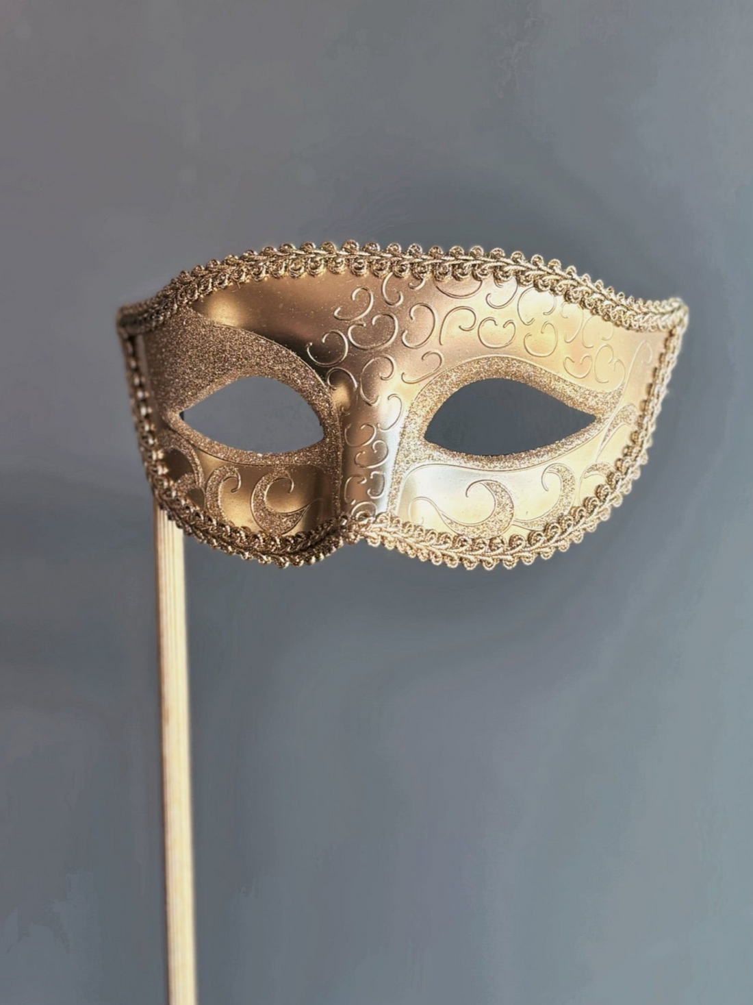 Gold handheld masquerade mask with ornate scroll design and stick handle